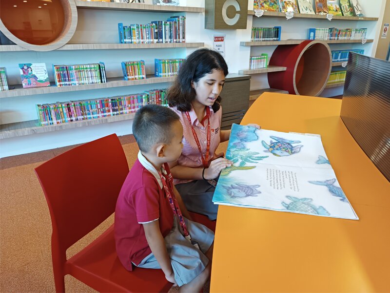 A Secondary student reading a book for the Early Years student